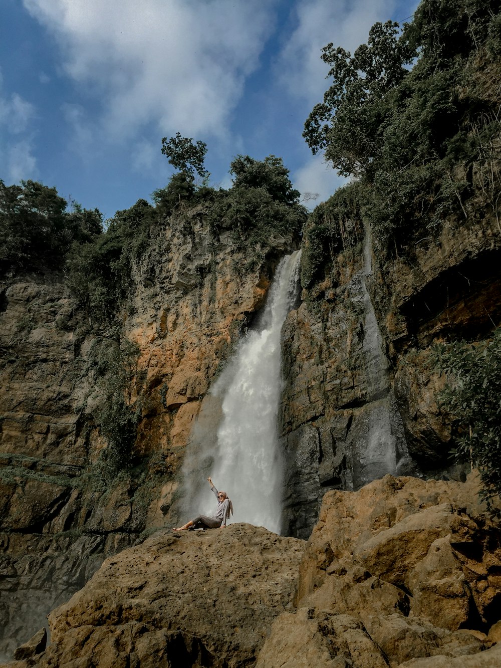 woman in red dress standing on brown rock near waterfalls during daytime