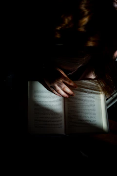 A cinematic close-up of a person reading a novel by soft window light.
