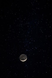 A glowing crescent moon surrounded by sparkling stars and zodiac symbols against a deep midnight blue background.