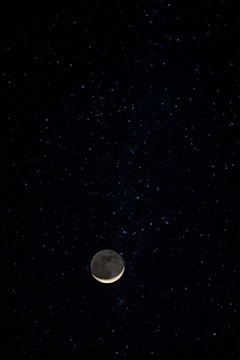 A glowing crescent moon surrounded by sparkling stars and zodiac symbols against a deep midnight blue background.