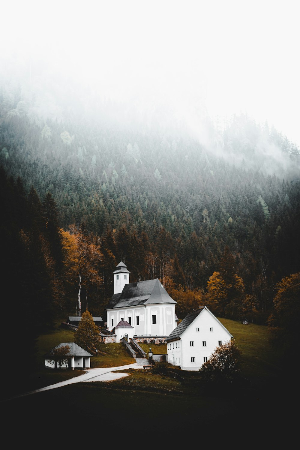 white and brown house near green trees under white sky during daytime