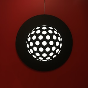 A sleek modern light fixture casting sharp red and grey shadows on a textured black wall