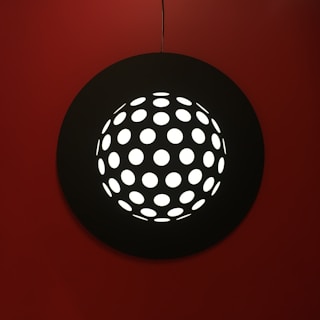 A sleek modern light fixture casting sharp red and grey shadows on a textured black wall