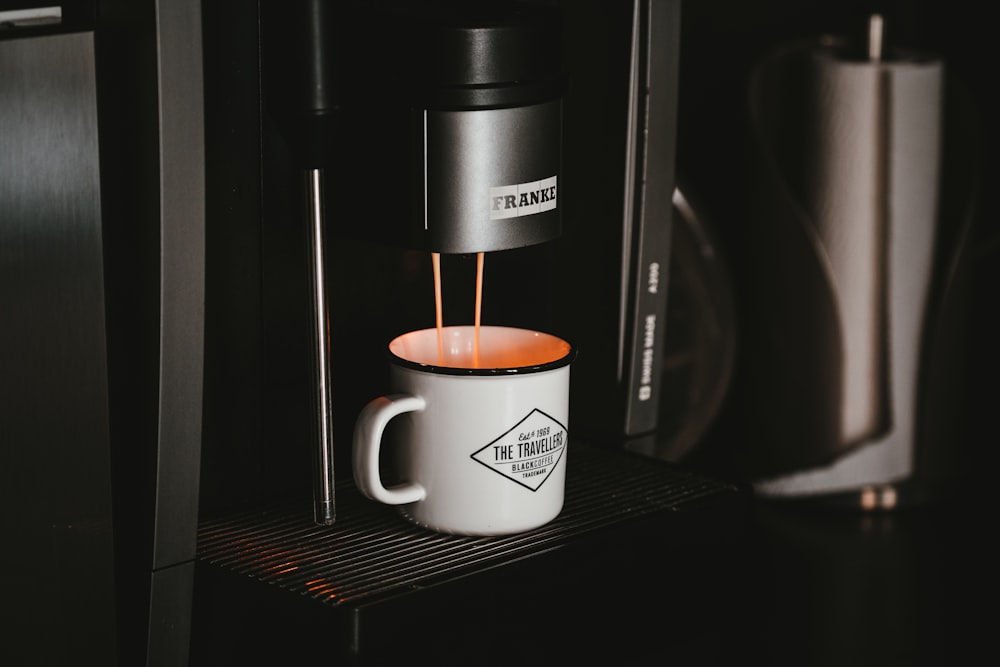 Taza de cerámica blanca en cafetera negra y plateada