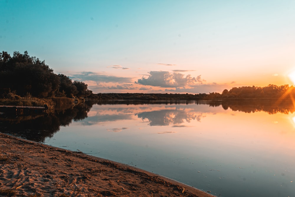 body of water near trees during sunset