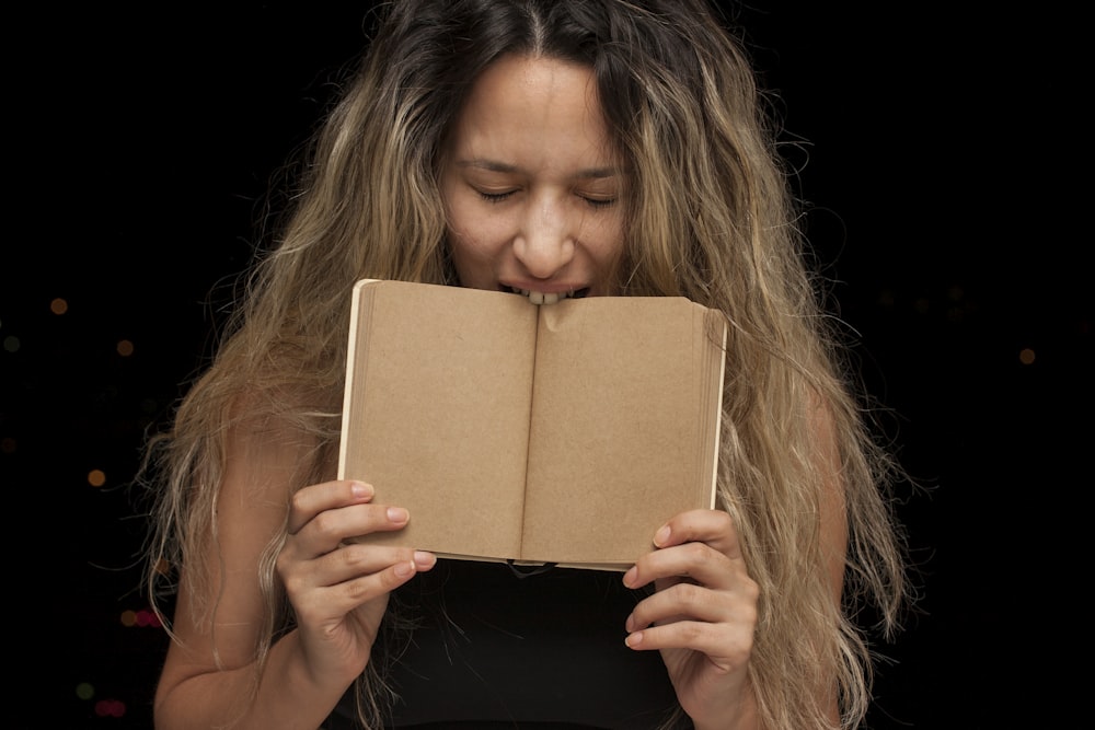 mujer cubriendo su cara con un libro marrón