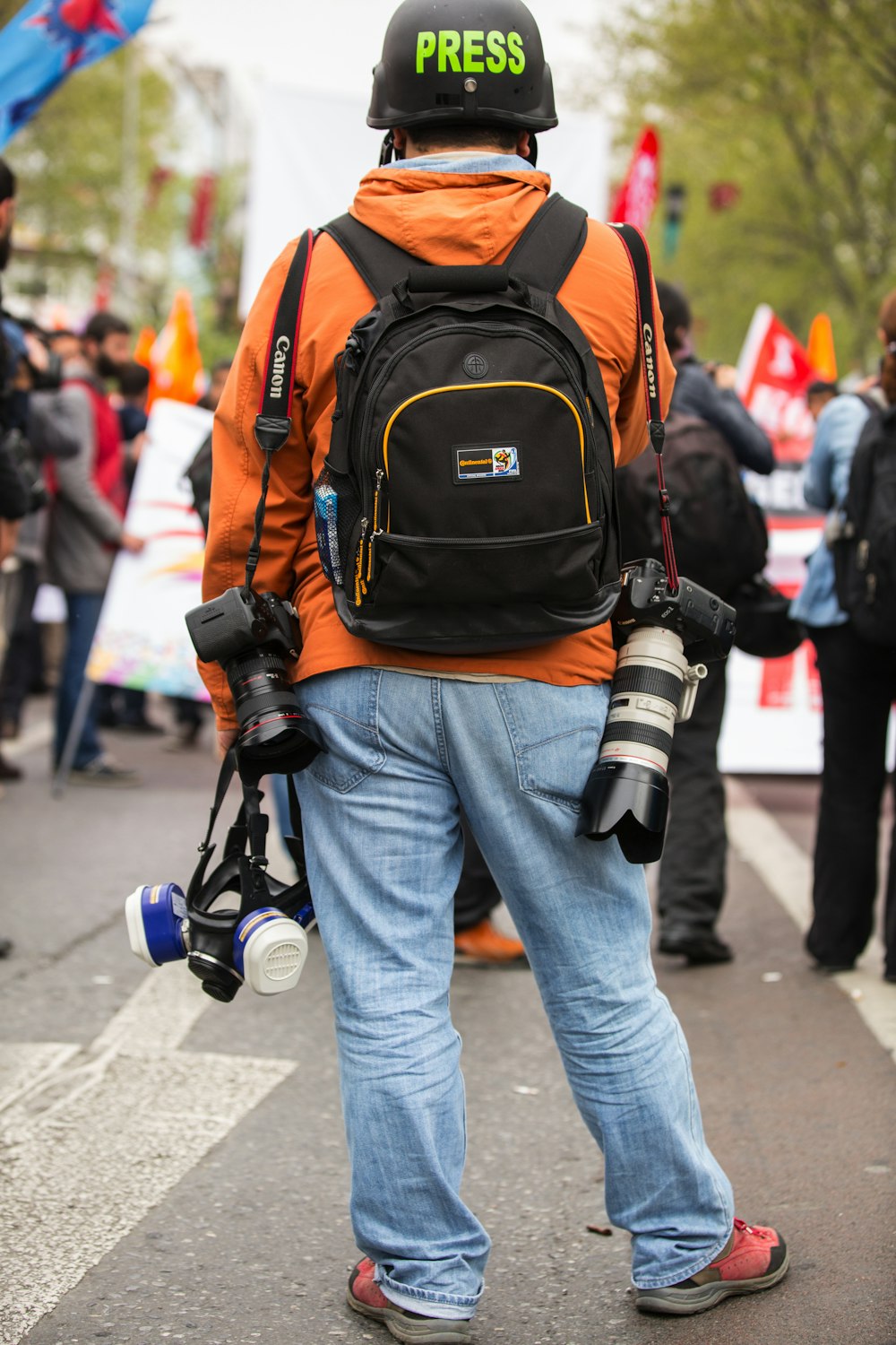 ブルーデニムのジーンズとオレンジ色のリュックサックを背負った人が昼間、通りを歩いている