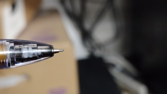 A close-up view of a ballpoint pen tip with the internal mechanism visible. The background is blurred, emphasizing the pen.