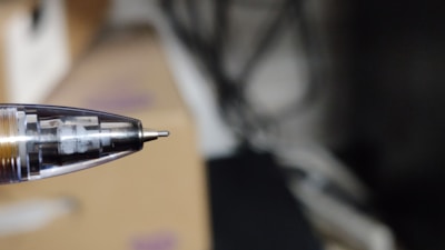 A close-up view of a ballpoint pen tip with the internal mechanism visible. The background is blurred, emphasizing the pen.