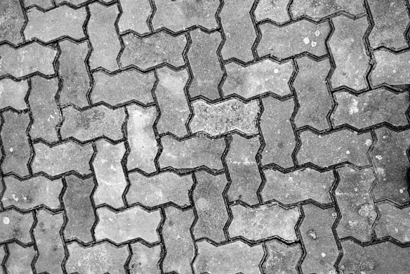 Interlocking pavers with a distinctive zigzag pattern cover a surface, showing signs of wear and some discoloration.