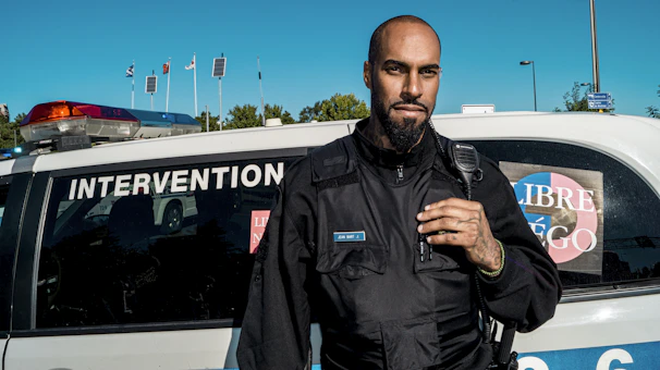 A police actor in full uniform standing confidently beside a vintage patrol car on a film set