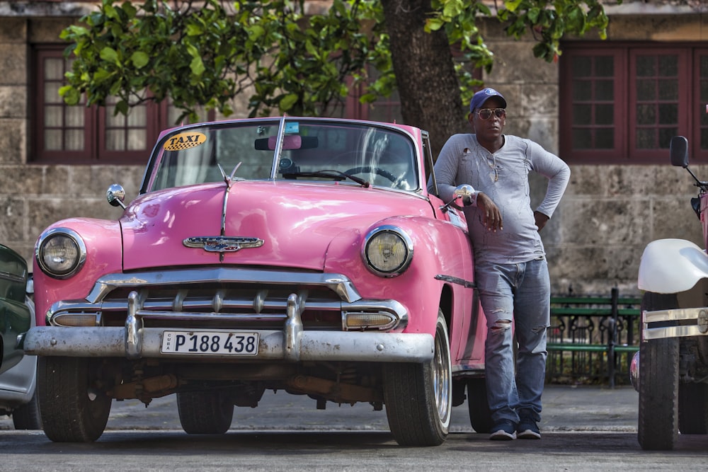 homem na camisa social branca e jeans azul de pé ao lado do carro rosa durante o dia