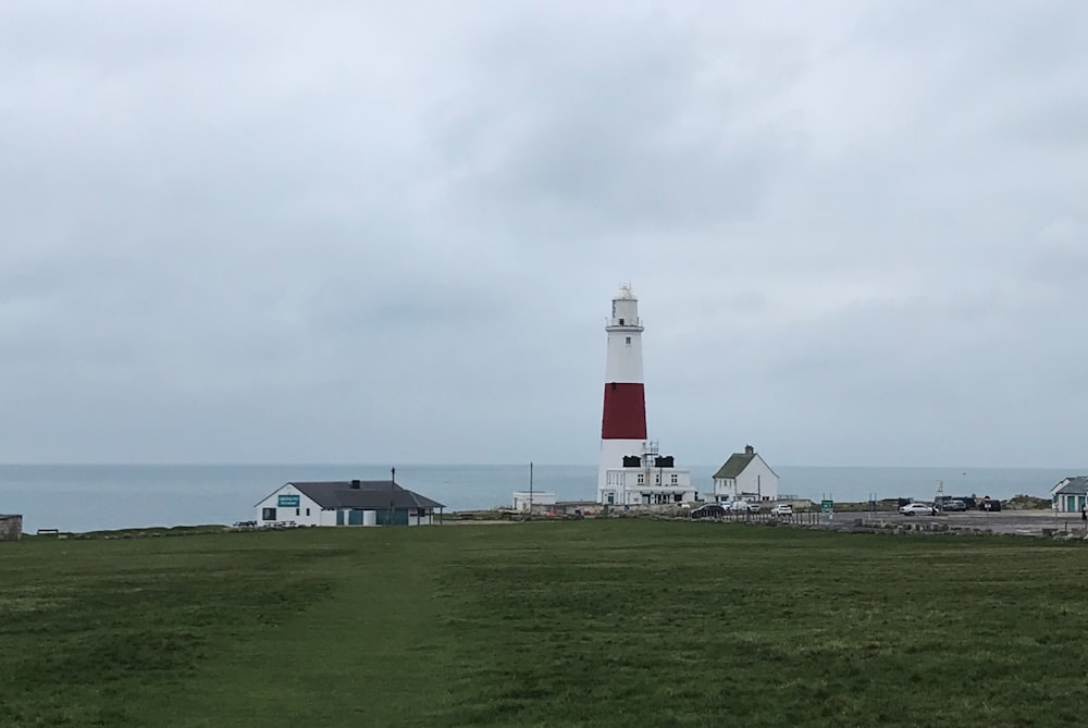 white and red lighthouse on green grass field under white cloudy sky during daytime