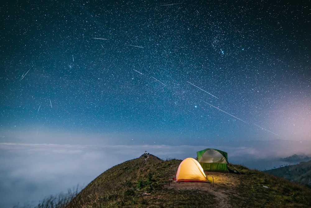 tenda gialla sul campo di erba verde sotto il cielo blu con le stelle durante la notte