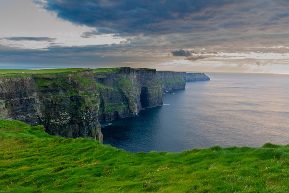 Champ d’herbe verte à côté d’un plan d’eau sous un ciel nuageux pendant la journée