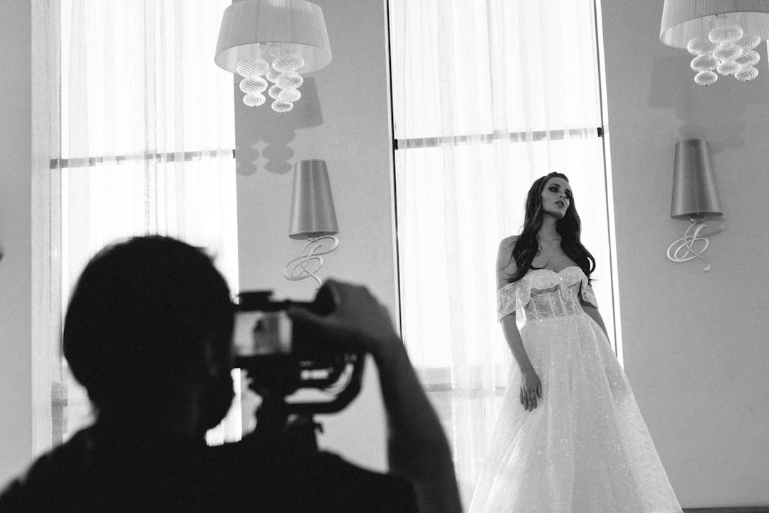 grayscale photo of woman in white dress holding camera