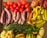 A collection of various fresh vegetables arranged together, including red tomatoes, purple-striped eggplants, yellow-green peppers, and sweet potatoes. There are also other vegetables such as bitter melon, cauliflower, and green chili peppers, as well as striped melons.