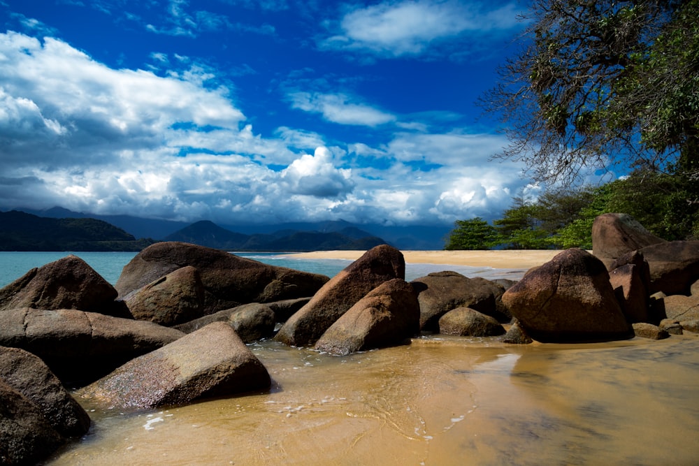 brown and gray rocks on body of water under blue and white cloudy sky during daytime