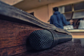 A sleek black and gold microphone resting on a dark wooden table, glowing softly under moody lighting.