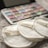 Three cream-colored reusable cotton pads with the label 'EcoPanda™' are placed on a soft, textured surface. In the background, a palette of watercolors or makeup shows assorted hues, slightly out of focus.