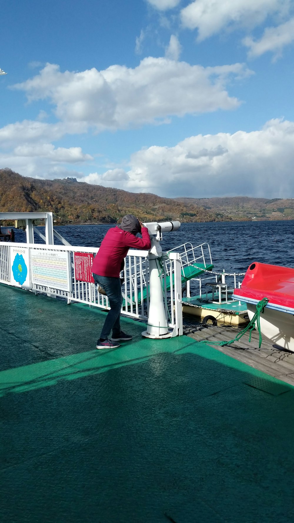 mujer con camisa roja de manga larga y pantalones grises de pie en un barco verde y blanco durante