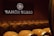 A dimly lit room filled with rows of wooden wine barrels, each marked with the brand name. A large illuminated sign displaying 'Ramón Bilbao' is mounted on the wall above the barrels, adding to the atmosphere.