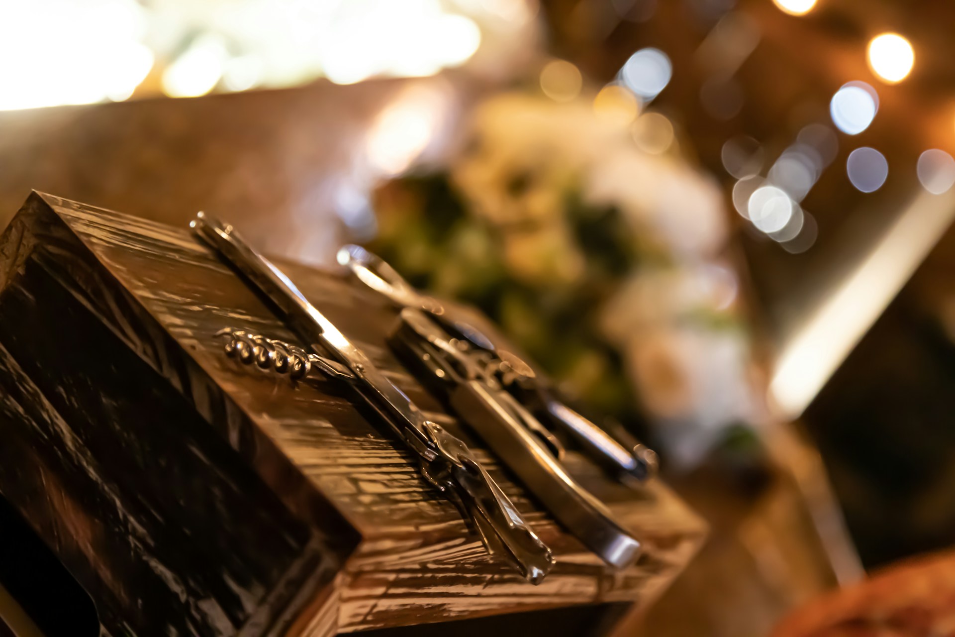 A set of shiny metal corkscrews and bottle openers rests on a wooden surface, with a soft background of warm bokeh lights creating a cozy ambiance.