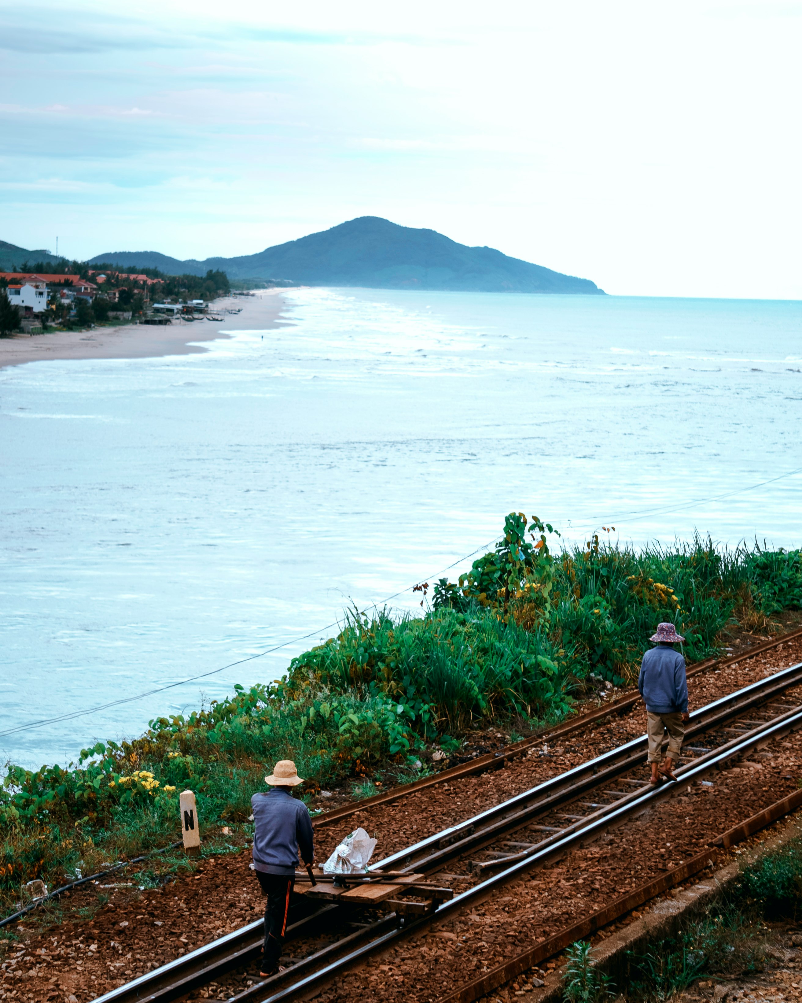 man and woman walking on train rail near body of water during daytime