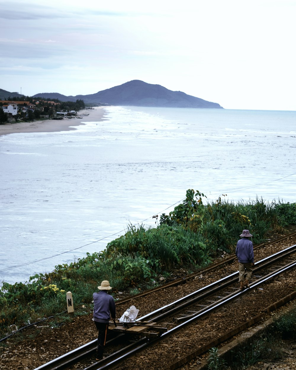 man and woman walking on train rail near body of water during daytime