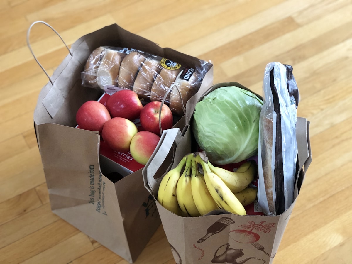 Paper grocery bags filled with fresh fruits, vegetables, and bread representing online grocery delivery