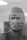 A medical professional is seen wearing a surgical mask and cap, with a reflective surface showing blurred text in the foreground. The image is captured in black and white, giving it a classic and serious tone.