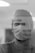 A medical professional is seen wearing a surgical mask and cap, with a reflective surface showing blurred text in the foreground. The image is captured in black and white, giving it a classic and serious tone.