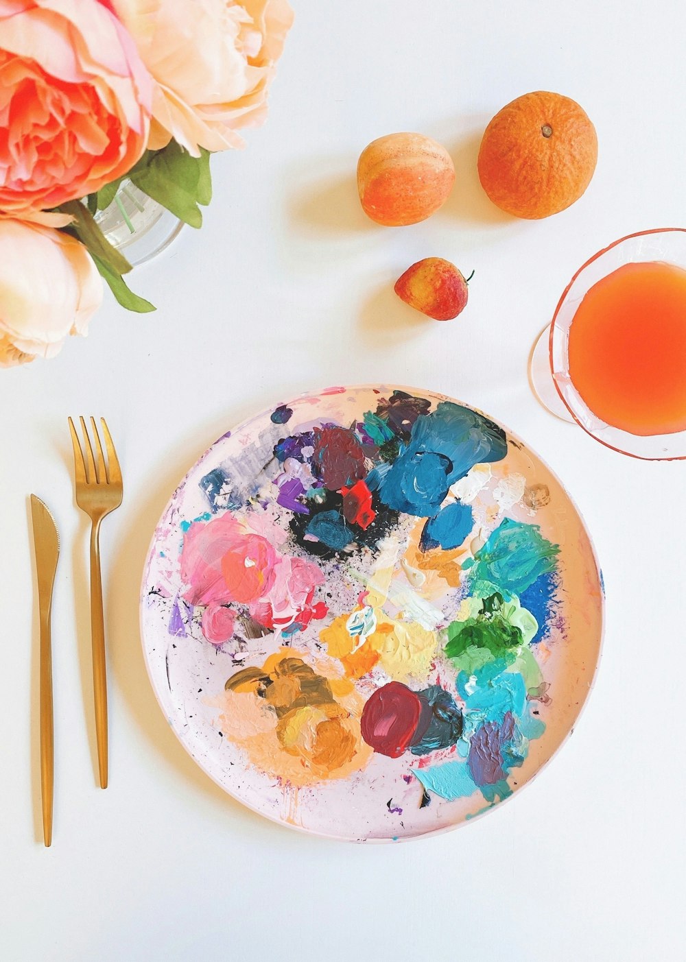tavolozza di colori con vernice su piastra di ceramica bianca accanto a forchetta e coltello d'argento