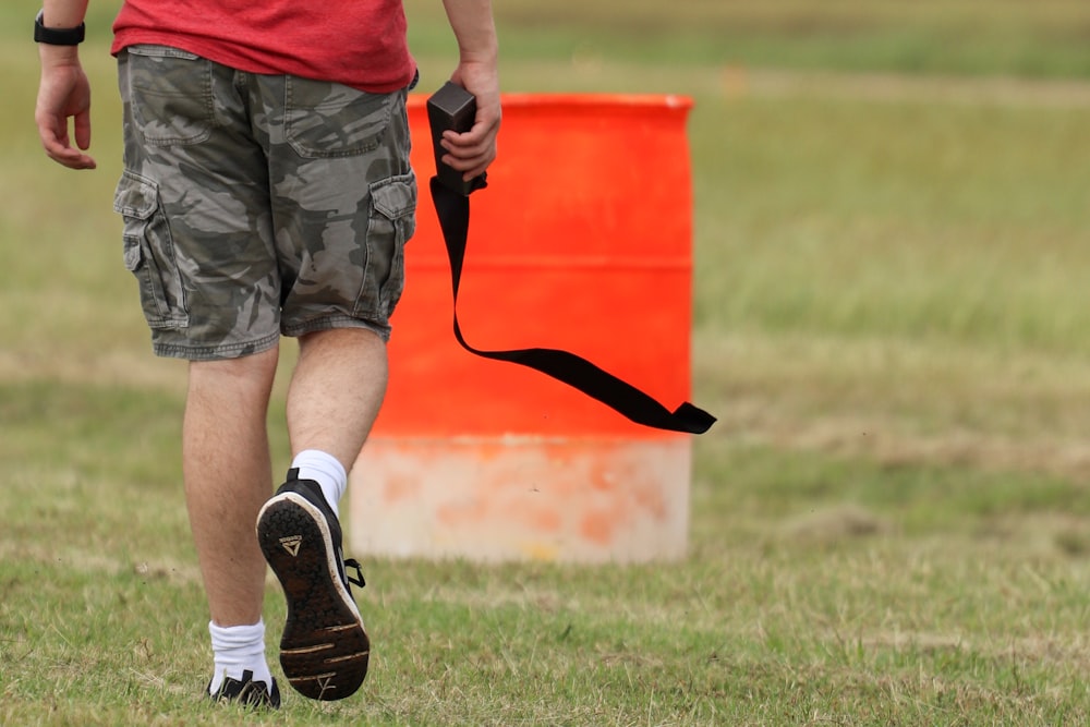 man in red shirt and black shorts with black and white nike sneakers standing on green