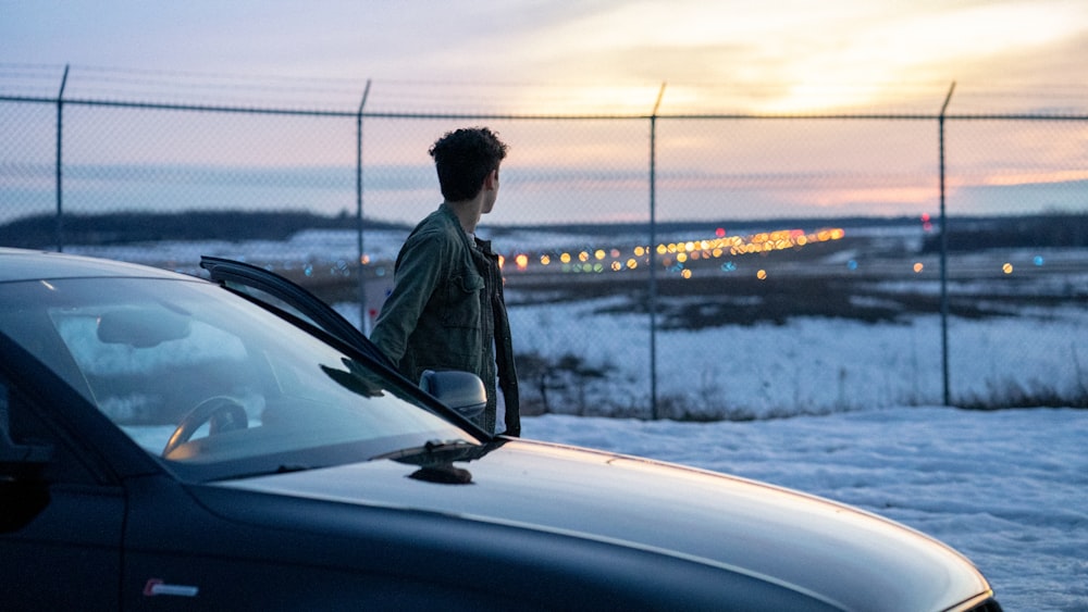 man in black jacket standing beside car during daytime