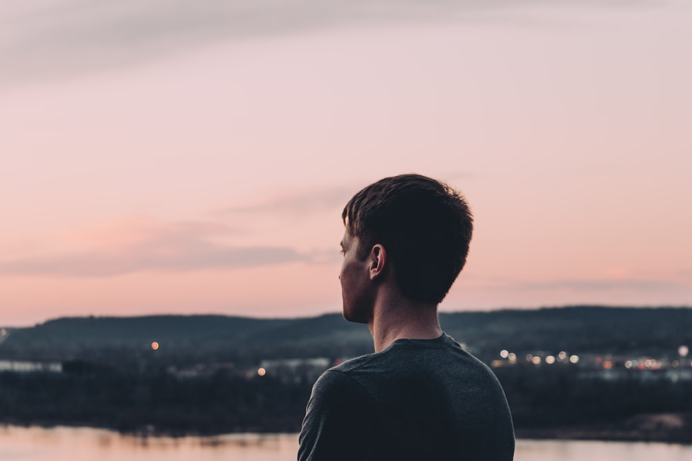 man in black shirt standing near body of water during sunset