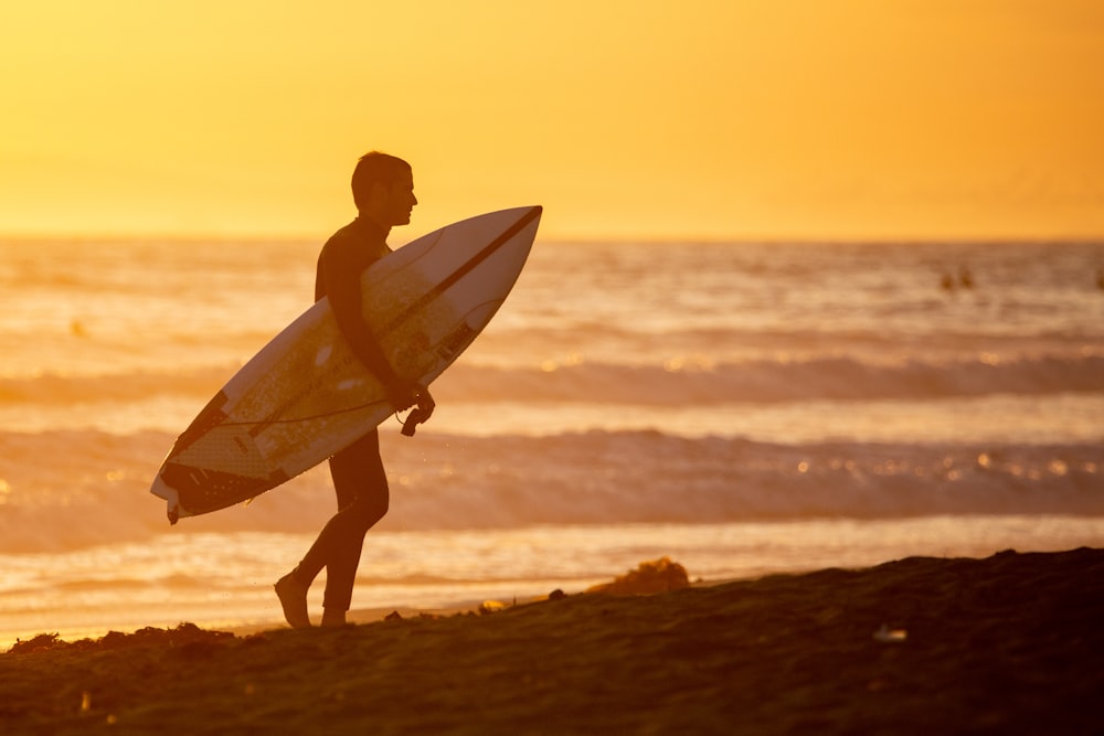 man in yellow shirt holding white surfboard walking on seashore during daytime