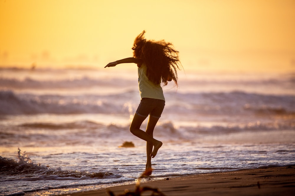 woman in white shirt and white shorts walking on beach during sunset