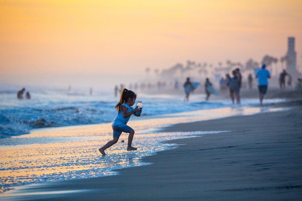 chica con camisa azul y blanca corriendo en la playa durante el día