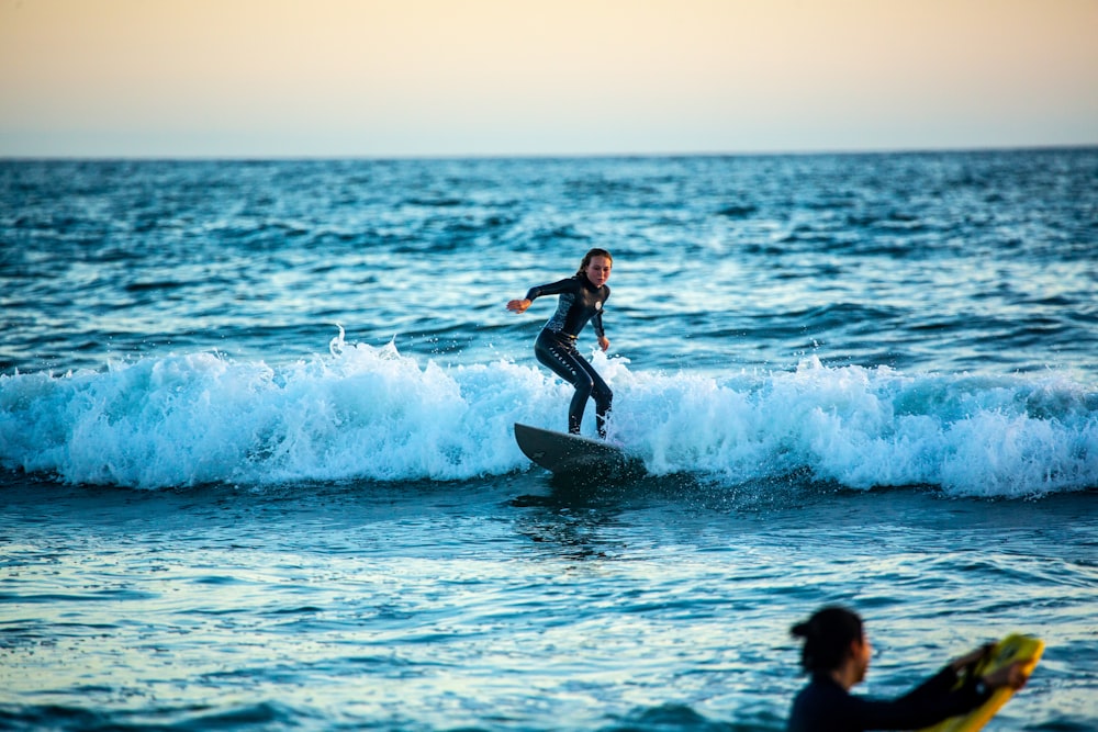 woman in black wetsuit surfing on sea waves during daytime