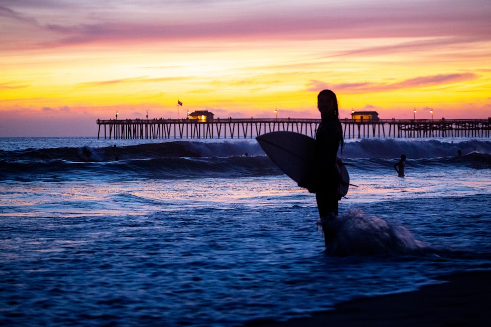 silhouette of person holding surfboard on beach during sunset