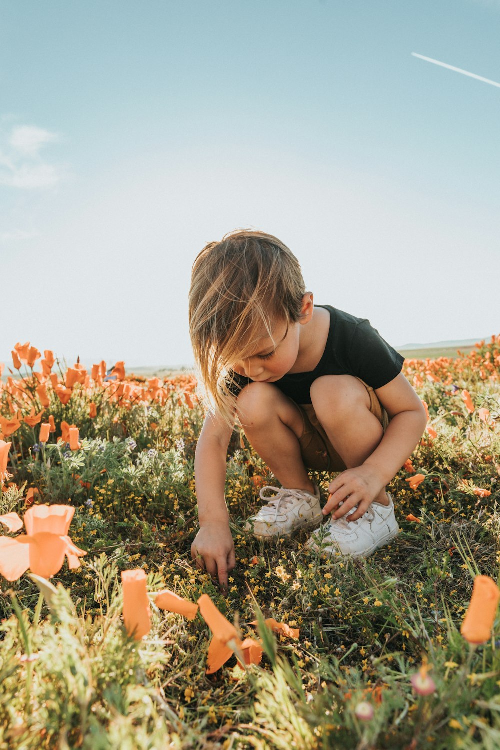 woman in black tank top sitting on ground surrounded by orange flowers during daytime