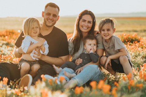 3 women and 2 men sitting on green grass field during daytime