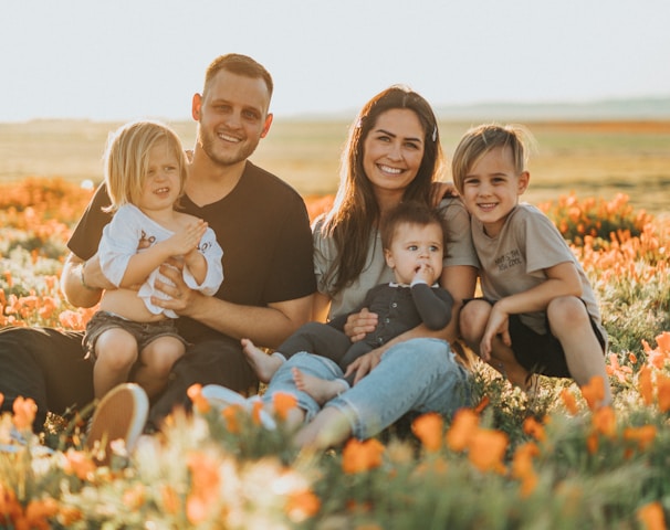 3 women and 2 men sitting on green grass field during daytime