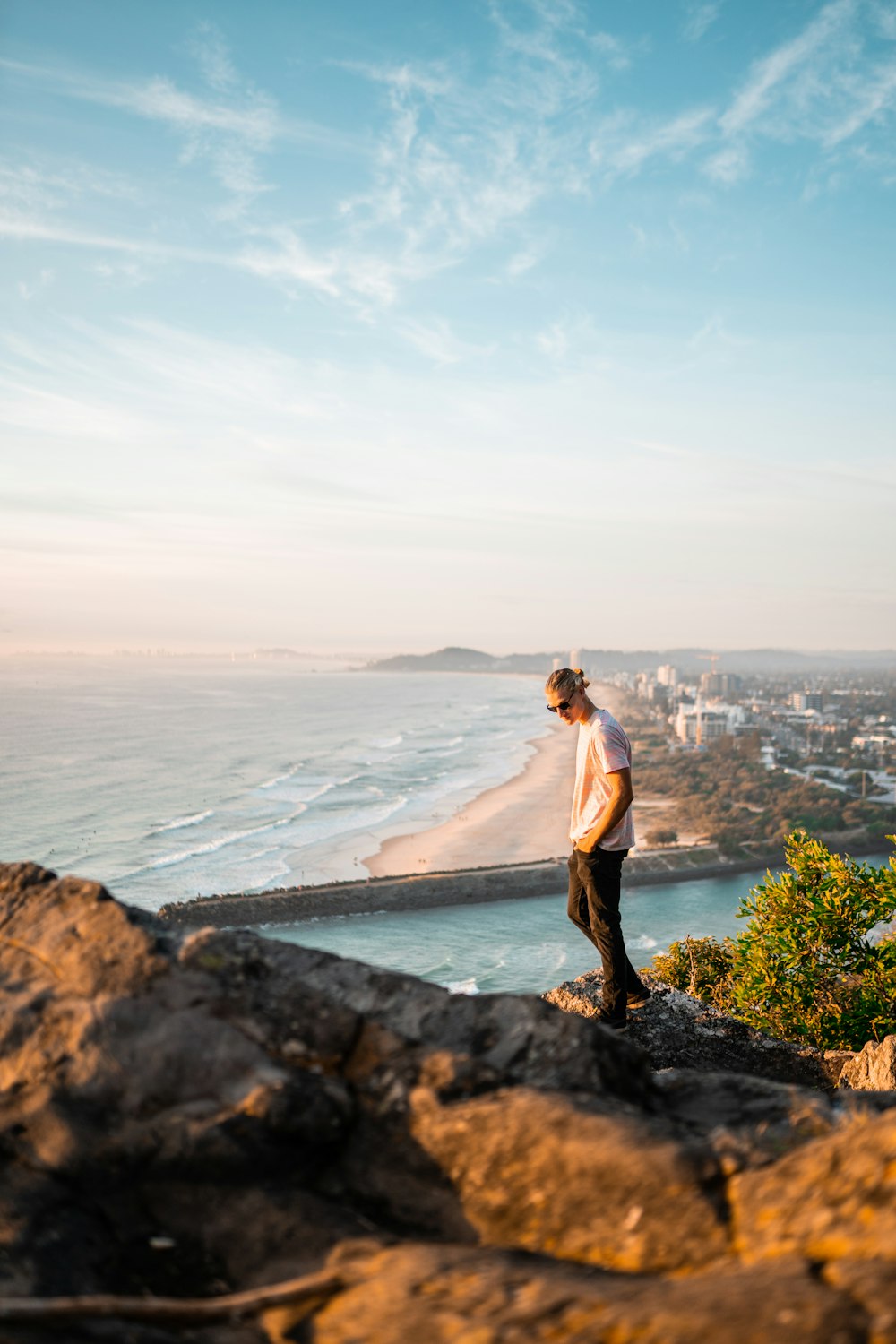 man in white tank top and black shorts standing on rock formation near body of water