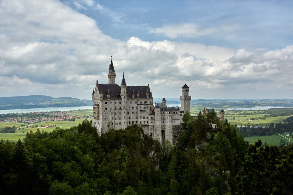 white and gray castle on top of green trees under white clouds and blue sky during