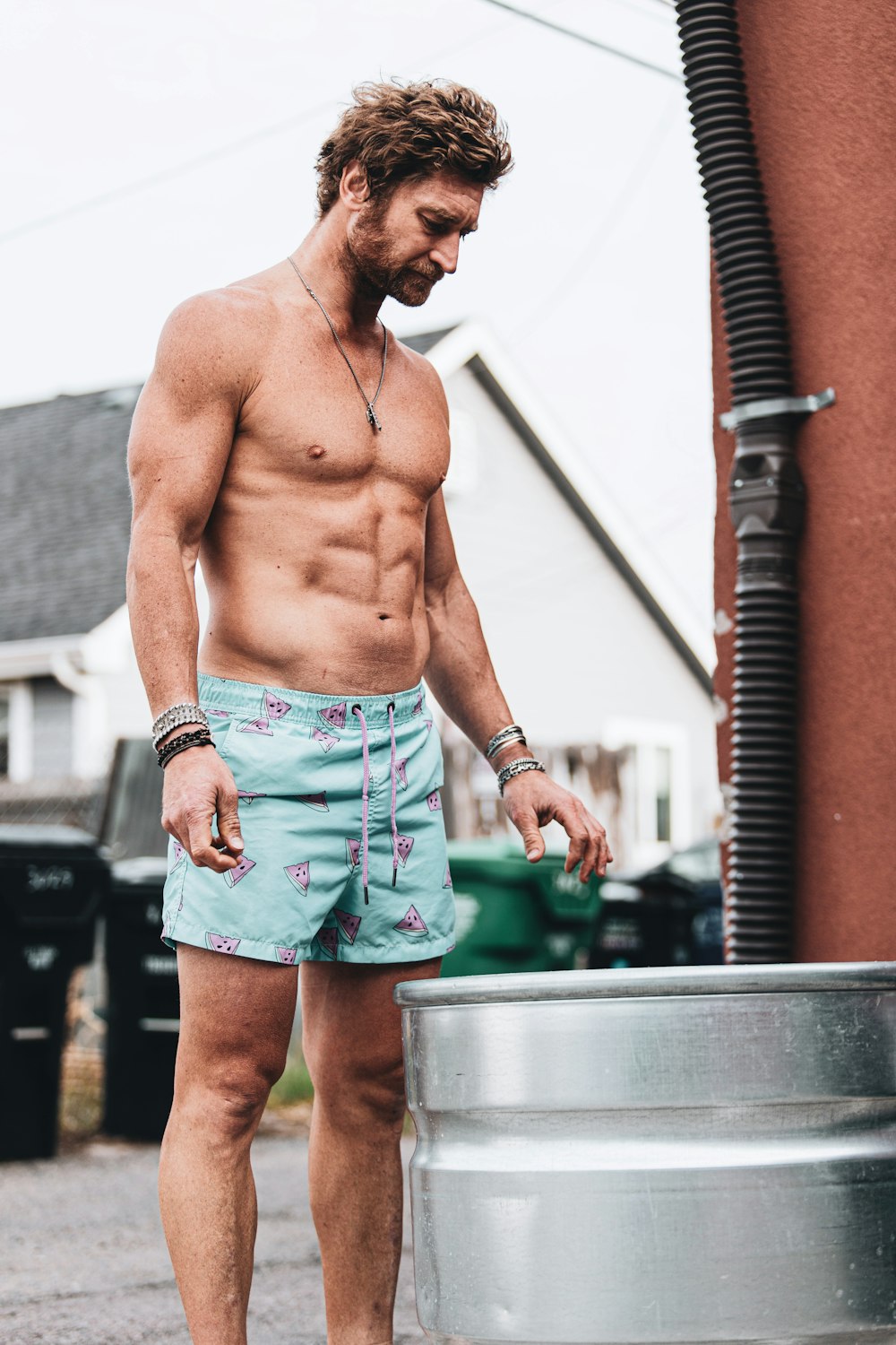topless man in blue denim shorts standing near brown brick wall during daytime