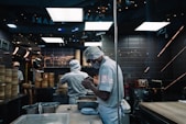 man in white long sleeve shirt and white pants standing in front of kitchen counter