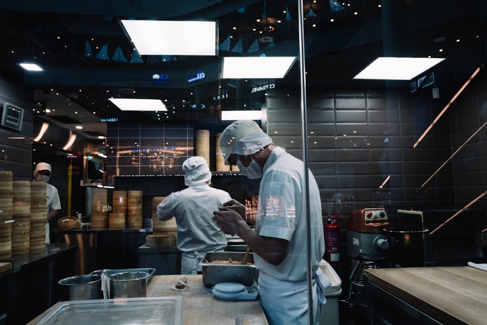 man in white long sleeve shirt and white pants standing in front of kitchen counter