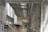 A spacious industrial facility with high ceilings and extensive use of metal and industrial materials. The interior is well-lit, featuring clean, organized rows of machinery and equipment. A single person is walking in the distance, emphasizing the scale of the space. The environment appears to be a manufacturing or industrial warehouse with marked walkways and large doors.